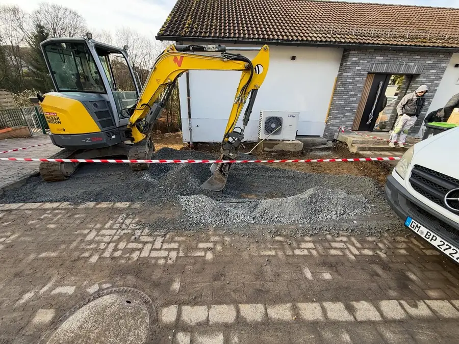 Bagger und frisch angelieferter Schotter vor einem Wohnhaus