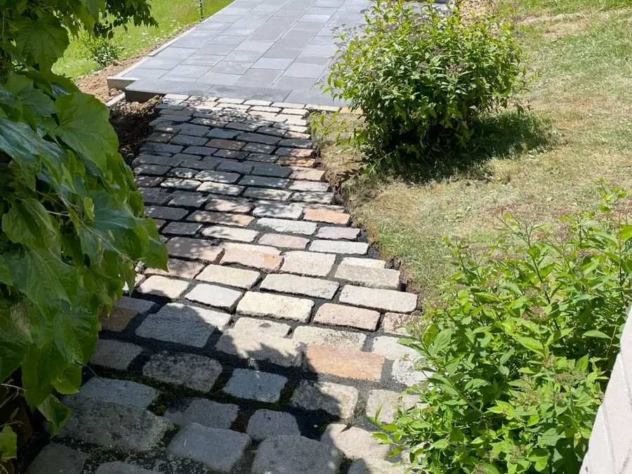 Gartenweg aus Kleinpflaster mit Plattenband, eingefasst von Grünflächen