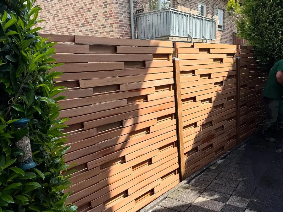 Neuer Sichtschutzzaun aus Holz neben einer gepflasterten Zufahrt